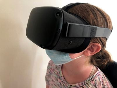 a young child wears a virtual reality headset and a surgical mask