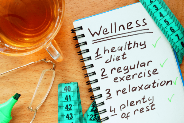 Notebook open with text: Wellness 1) healthy diet; 2) regular exercise; 3) relaxation; 4) plenty of rest