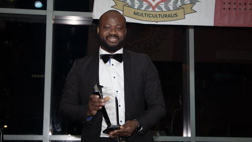 Michael Adjei, MD, a black man, is dressed in a tux and holding an award