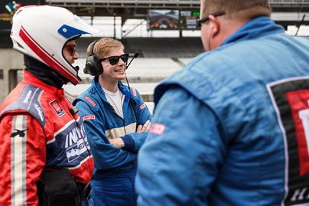 Leonard Edwards, in fire suit and helmet, talks with IU School of Medicine resident Justin Smith, in blue fire suit, and a member of the IndyCar safety team trackside on pit row.