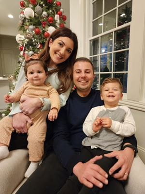 Lana Dbeibo and Nabil Adra with their two small children on their laps, in front of a Christmas tree