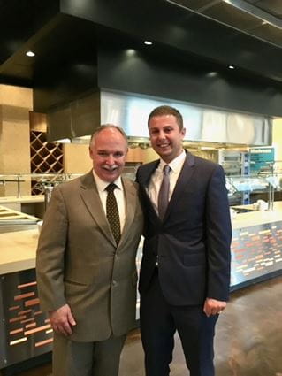 Patrick Loehrer and Nabil Adra stand side by side, wearing suits, inside a restaurant