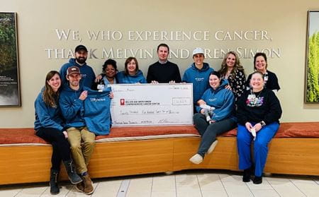 Nabil Adra with Hartnagel family members, wearing Stay Positive sweatshirts, and IU Health staff, at the cancer center, holding an oversized donation check