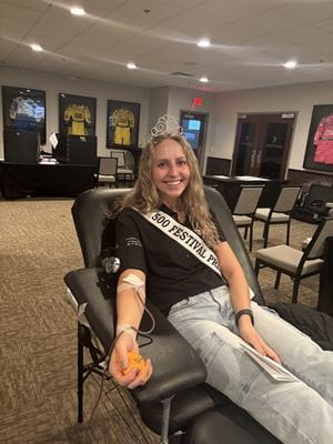 Elizabeth Baker, wearing her tiara and sash, in a chair at the Indianapolis Motor Speedway donating blood
