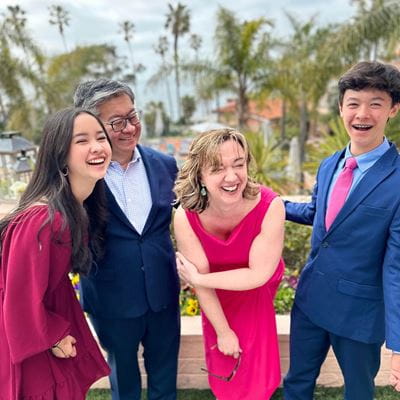 The Choi family laughs together outside, wearing semi-formal attire; (left to right) daughter, dad Alex, mom Jennifer, and their son.