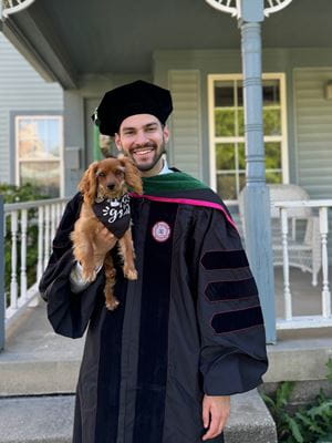 Devin Gantzios-Cros wears his graduation cap and gown and holds and his small dog, Match, outside his Indianapolis home.