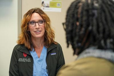 Dr. Kelly Kasper, wearing scrubs and IU logo jacket, talks with a Black patient in clinic
