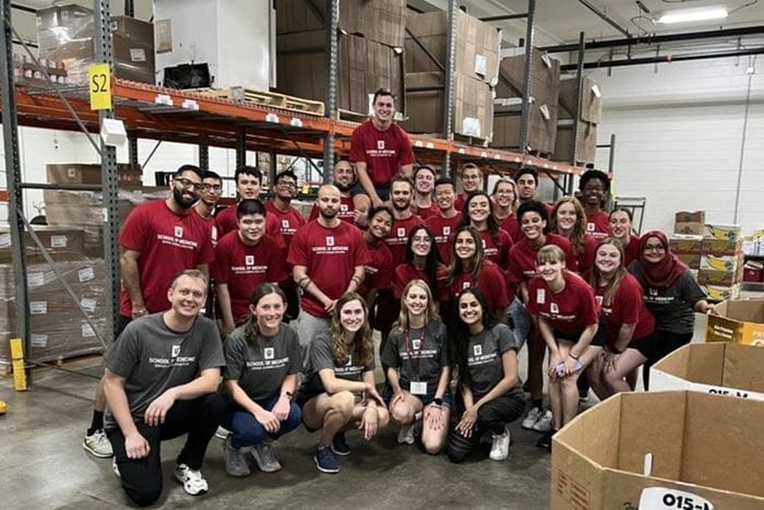 a large group of students in matching red tshirts gather in the food bank warehouse
