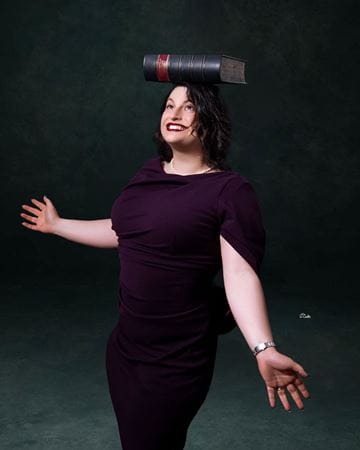 Hannah Kline in plum dress balancing a thick book on her head