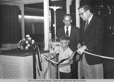 A child cuts the ribbon for an addition to Riley Hospital for Children with assistance from Walter Daly and David Handel, representing IU School of Medicine and IU Hospitals