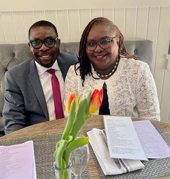 Kola Okuyemi sits with his wife, Funke, dressed in nice clothing, at a dining table with flowers