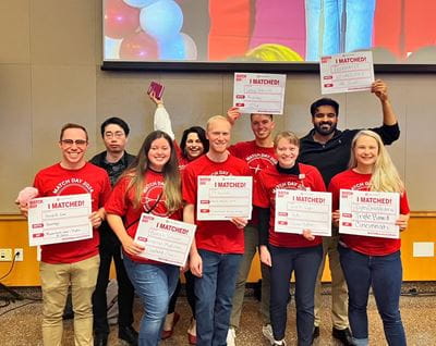 Nine students from the Medical Scientist Training Program in red Match Day shirts pose with their signs showing where they matched.