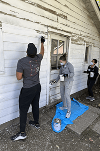 Three NeighborLink volunteers paint in the side of a building.
