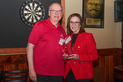 Dean Jay Hess, in red shirt, stands next to Maria Del Rio Hoover, in red jacket, holding her award trophy