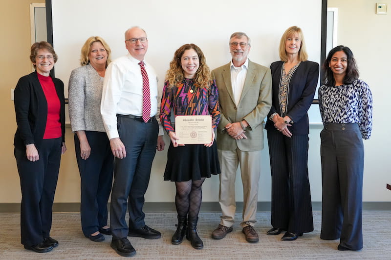 Emily Sims holds her Showalter Award certificate standing with six IU School of medicine leaders in a conference room
