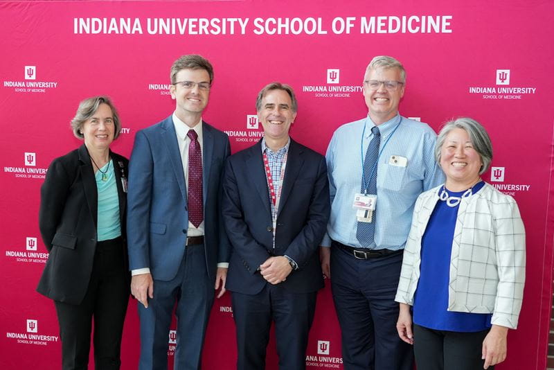 Five faculty members in front of a red IU School of Medicine logo backdrop at the Spring 2024 All School Meeting reception.