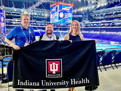 Steve Hartsock, Damon Martin and Kimbre Zahn hold an Indiana University Health banner near the pool deck at Lucas Oil Stadium