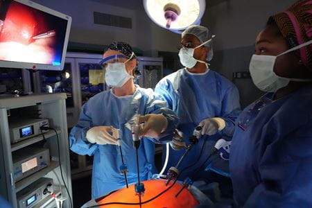 Dr. Choi and two trainees wear surgical scrubs and mask as they use probes to see images on screen during a surgery simulation.