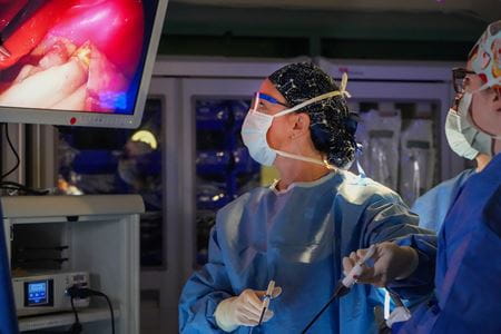 Jennifer Choi wears surgical scrubs and holds a probe; image of organs is displayed on a screen as trainees in foreground watch the procedure.