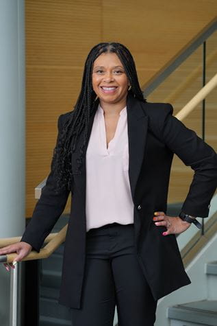 Tamika Dawson-Knox in black suit with hand on hip, leaning on staircase rail