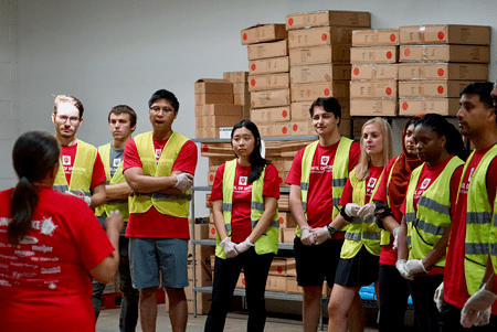students in red t-shirts and yellow safety vests listen to instructions from a leader at the food bank in gary