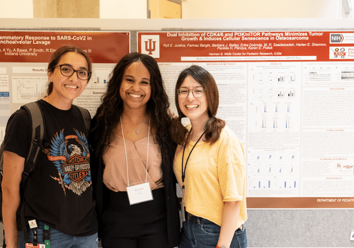 Three female students pose in front of a poster during an MPSEC poster session in 2022