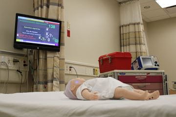 An infant patient mannequin lying on a hospital bed.