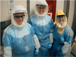 Melissa Kacena poses with two other researchers. All three people are smiling and wearing protective coverall suits.