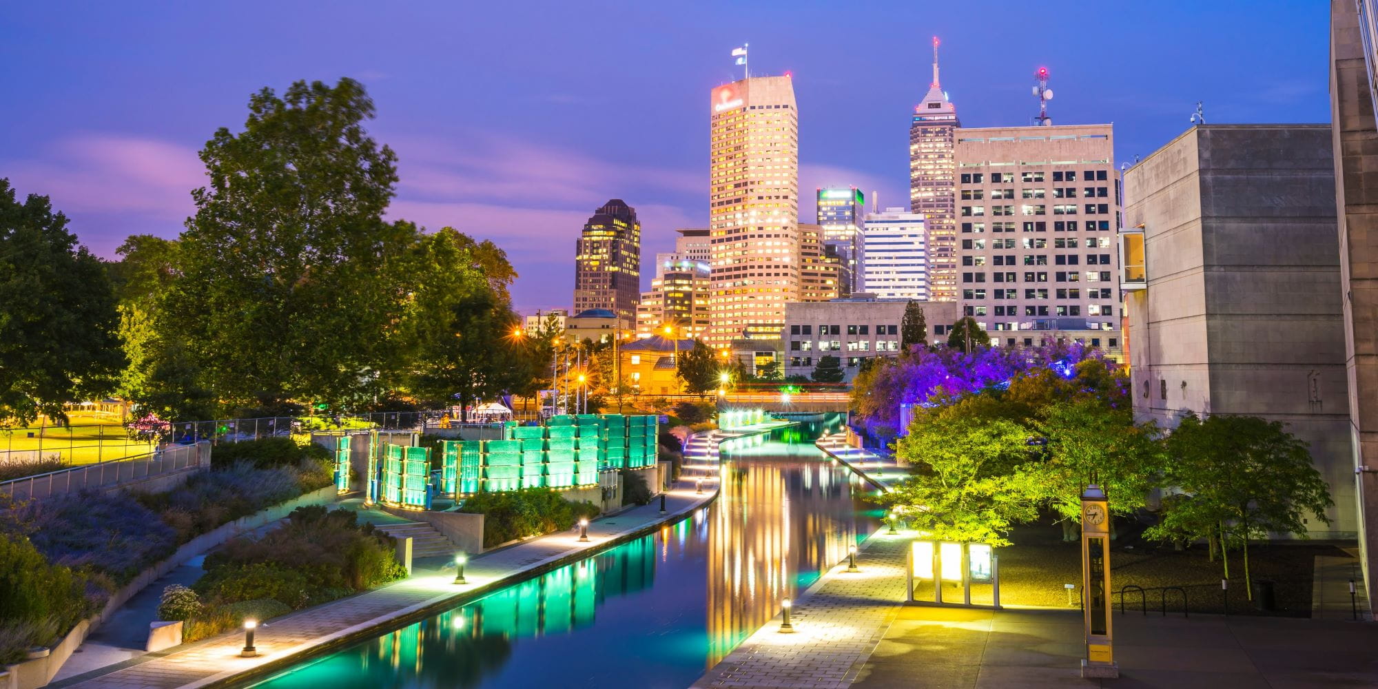 the indianapolis skyline is lit up at sunset rising over the downtown canal.