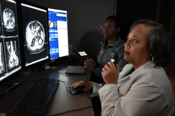 a resident and faculty member review radiology results on a bright monitor in a dark room