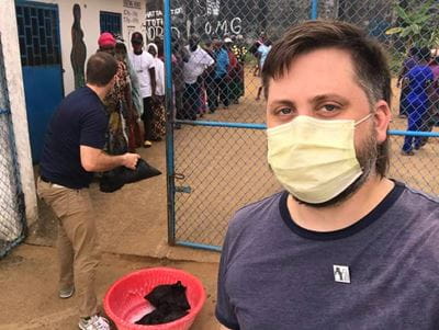 A photo of Dr. Michael Davis, wearing a face mask, standing in front of a line in Liberia.