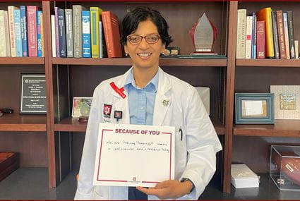 subha raman wears a red ribbon and holds a sign to thank donors. the sign reads "we are training tomorrow's leaders in cardiovascular care and research."