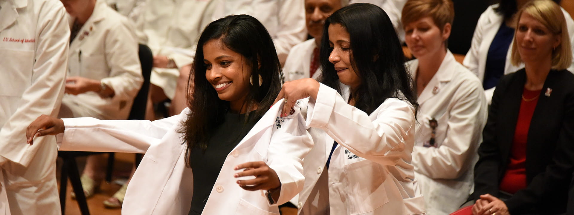 a faculty member puts a white coat on a new student